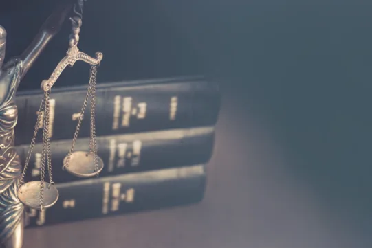 A metal statue of Lady Justice holding balanced scales stands in front of three stacked law books on a blurred background.