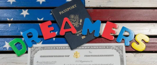 A U.S. passport, a certificate, and colorful letters spelling “DREAMERS” are arranged on an American flag background.