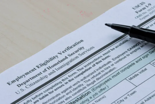 A close-up of a pen resting on a U.S. Department of Homeland Security Employment Eligibility Verification form.
