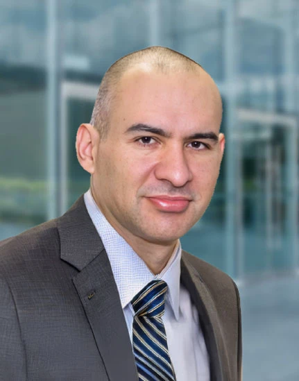 Marisol L. Pérez A man in a suit and striped tie stands in front of a glass building, looking at the camera with a neutral expression.