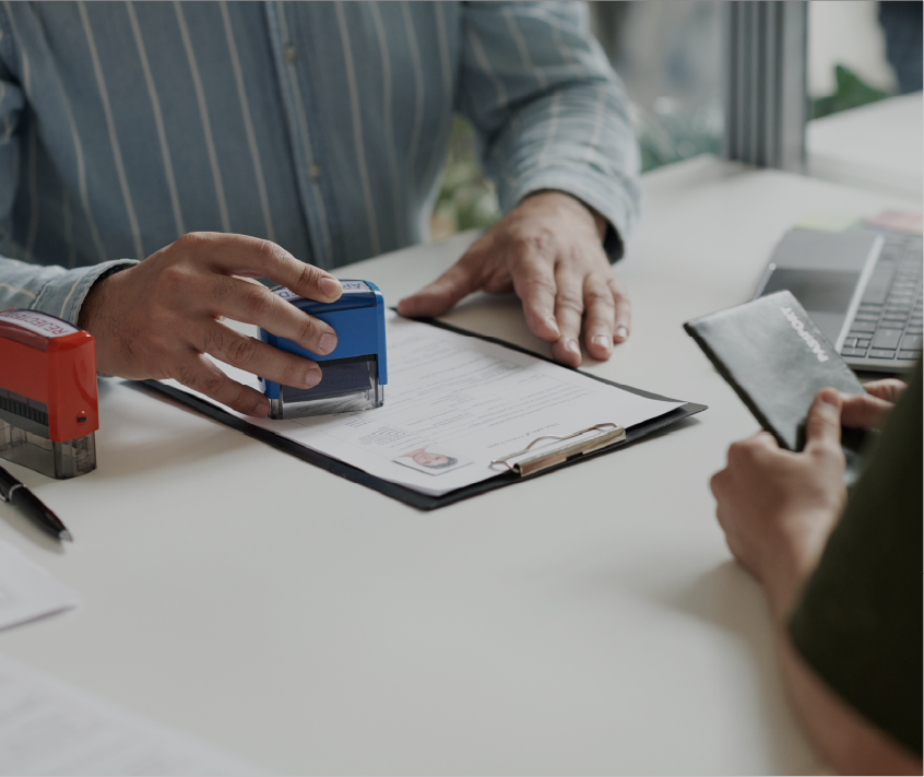 Person in striped shirt stamping a document on a clipboard while another person holds an ID card across the table.