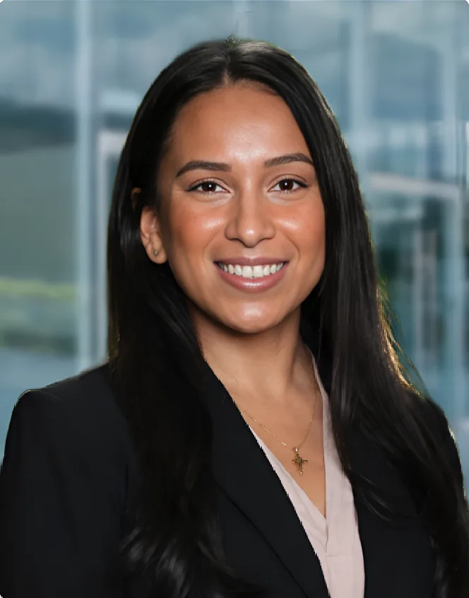 Marisol L. Pérez Woman with long dark hair wearing a black blazer and light blouse, smiling in front of a blurred glass building background.